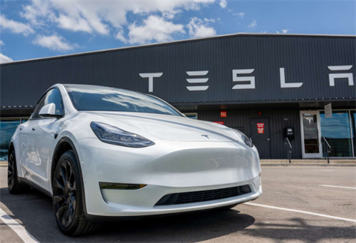 A white Tesla Model Y parked outside a dealership, representing Tesla's full-stack software-first autonomous driving strategy.